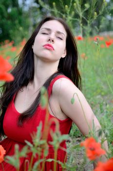 Charming girl surrounded by poppies. Female model with closed eyes, girl wearing red dress.