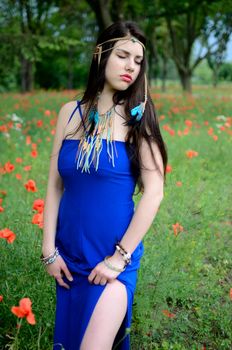 Relaxed girl with closed eyes. Female model with blue dress stands in meadow surrounded by flowers.