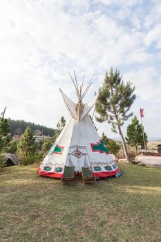 An indian teepee set up in a meadow among pine wood