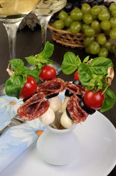 Appetizer of salami with mozzarella, olives, cherry tomatoes on skewers with basil