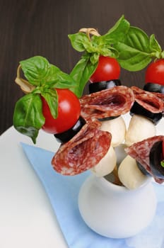 Appetizer of salami with mozzarella, olives, cherry tomatoes on skewers with basil