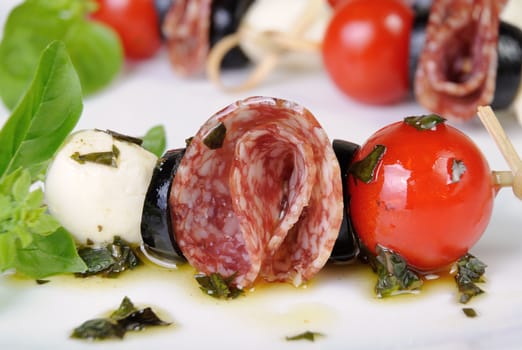 Appetizer of salami with mozzarella, olives, cherry tomatoes on skewers with basil oil