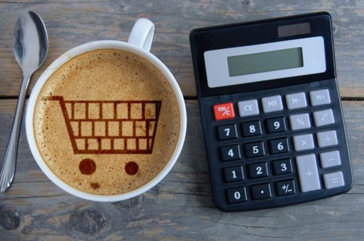 Shopping cart symbol inside a coffee cup by a calculator