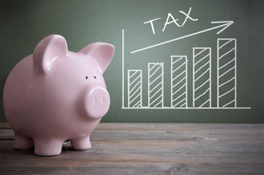 Chalk board tax chart with arrow pointing upwards by a piggy bank