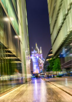 Blurred view of illuminated Tower Bridge framed by buildings reflections.