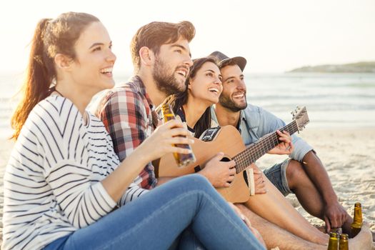 Friends having fun together at the beach, playing guitar and drinking beer