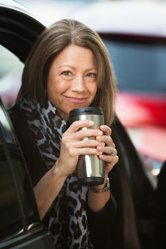 Cheerful mature adult woman holding coffee thermos