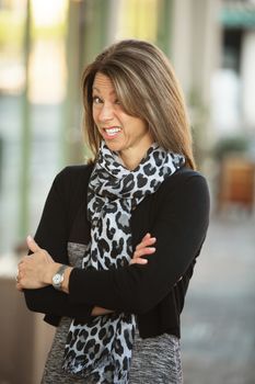 Single cringing businesswoman with folded arms standing outdoors