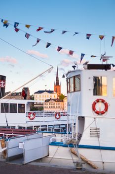 Swedish capital Stockholm in sunset. White traditional wooden  ferry steamer and old medieval downtown of Gamla stan in the background. Focus on background. Vertical composition.