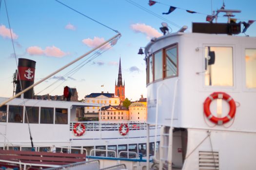 Swedish capital Stockholm in sunset. White traditional wooden  ferry steamer and old medieval downtown of Gamla stan in the background. Focus on background. Horisontal composition.