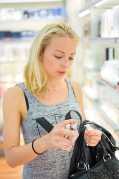 Casual blond young woman smelling perfume in retail store. Beautiful blond lady testing  and buying cosmetics in a beauty store.