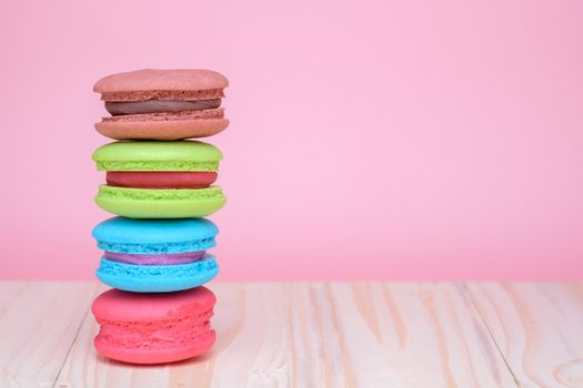 Sweet and colourful french macaroons on wooden table and pastel pink background