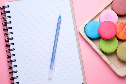Notebook and sweet dessert macaroon on pink background