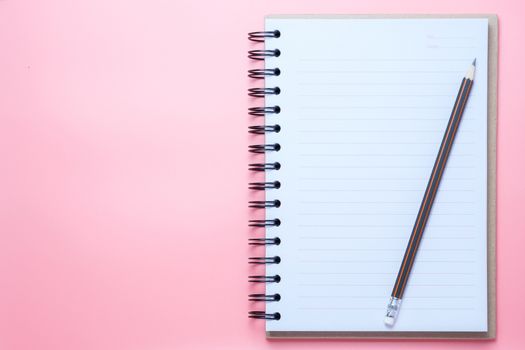 Notebook and pencil on pink background.
