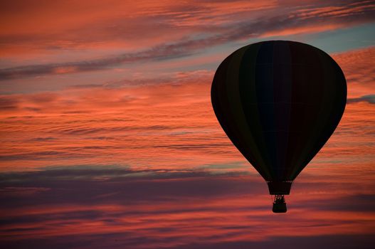 Hot-air balloon floating among pink and orange clouds at dawn