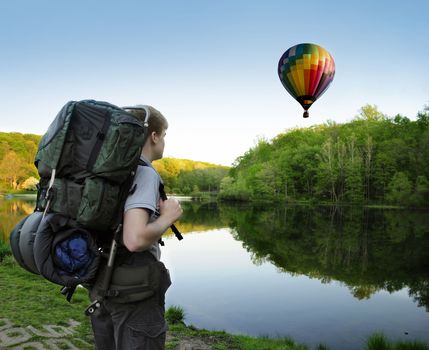 Backpacking hiker encounters a hot air balloon floating above a lake or pond