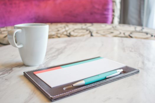 Notebook and white coffee cup on marble table
