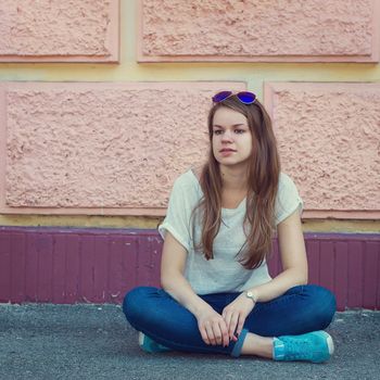 Girl in a T-shirt and jeans sitting on the pavement
