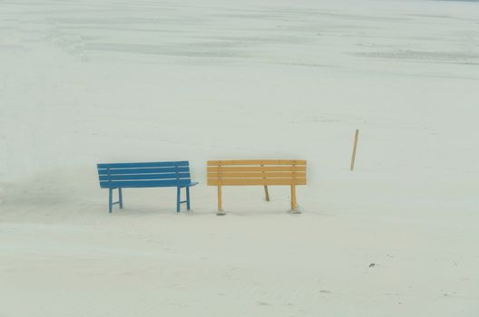 A blue and a yellow seat bench left on the beach at a Sandstrum.