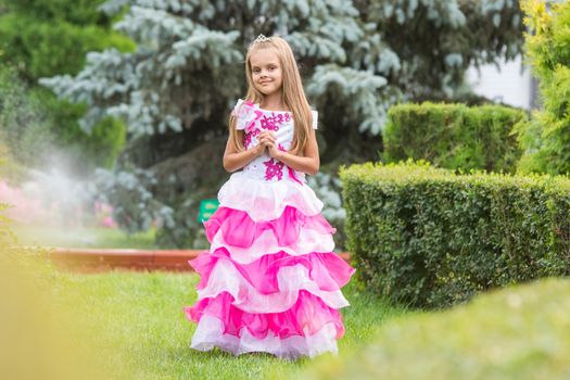 Happy six year old girl in a lush evening pink dress walking through the green garden