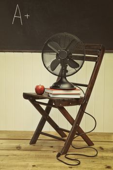 Old fan with apple and books on chair in school room