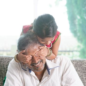 Happy Indian family at home. Asian girl surprising her father by covering daddy eyes. Parent and child indoor lifestyle.