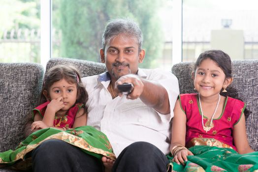 Happy Indian family watching tv together, father and children indoor living lifestyle at home.