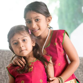 Indian girl hugging her younger sister with love. Asian children at home. Beautiful daughters in traditional India sari.