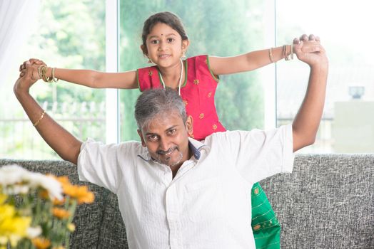 Happy Indian family at home. Asian parent playing with kid, sitting on sofa. Father and daughter indoor lifestyle.