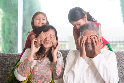 Indian family living lifestyle at home. Cute girls in traditional sari costume covering father and mother eyes. Asian parents and children.