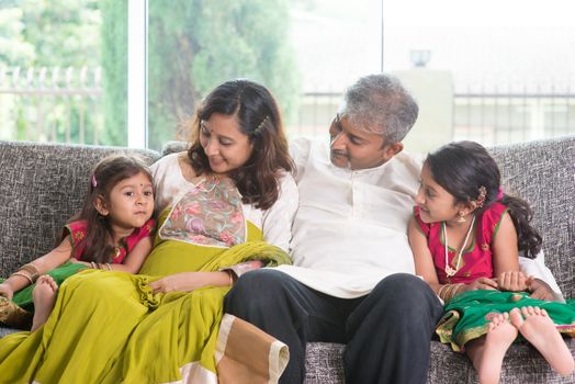 Happy Indian family at home. Asian parents bonding with their children, sitting on sofa. Adults and kids indoor lifestyle.