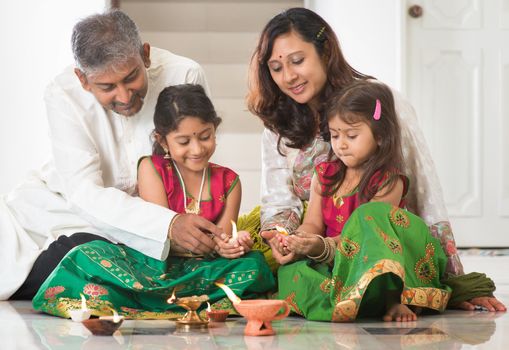 Indian family in traditional sari lighting oil lamp and celebrating Diwali, fesitval of lights at home. Little girl hands holding oil lamp indoors.