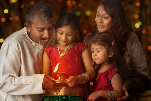 Indian family in traditional sari lighting oil lamp and celebrating Diwali, fesitval of lights inside a temple. Little girl hands holding oil lamp with beautiful bokeh background.