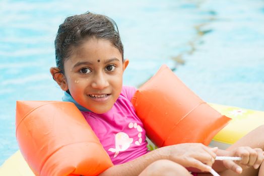 Cute Indian girl learning swimming in pool. Asian kid in swimmer class with float bands.
