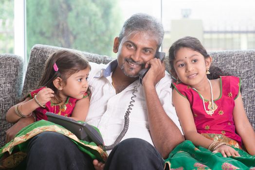 Daddy  making a phone call to mommy while taking care of children at home. Asian Indian family at home.