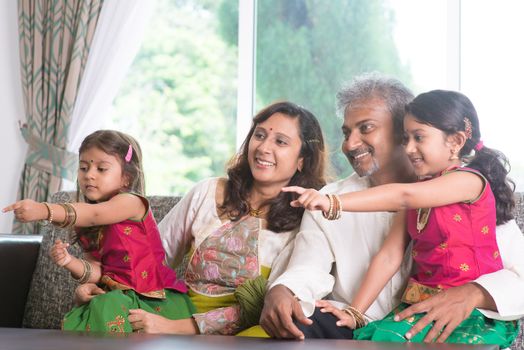 Happy Indian family at home. Asian people laughing and pointing to somewhere. Parents and children indoor lifestyle.