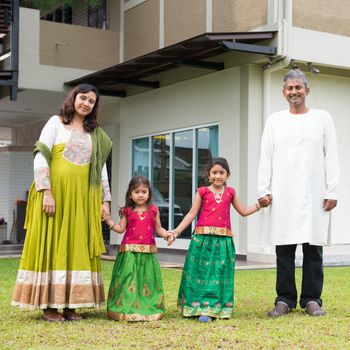 Indian family in traditional dress saree holding hands standing outside their new home.