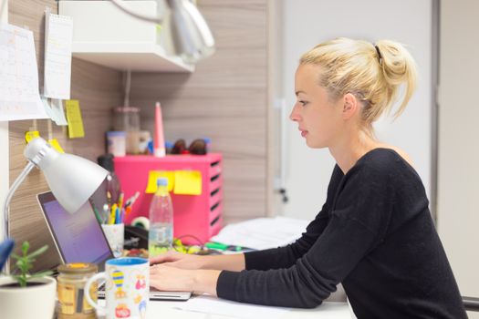 Business and entrepreneurship consept. Beautiful blonde business woman working on laptop in colorful modern creative working environment.