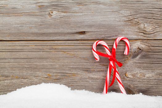 Colorful striped red and white Xmas candy canes with winter snow on wooden boards, with copyspace