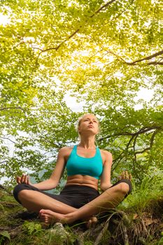 Relaxed woman enjoying freedom and life in beautiful natural environment. Blissful girl in lotus pose feeling relaxed, free and happy. Concept of freedom, happiness, enjoyment and natural balance.