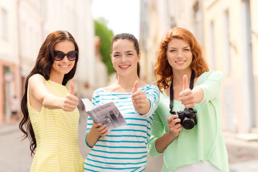 tourism, travel, leisure, holidays and friendship concept - smiling teenage girls with city guide and camera showing thumbs up outdoors