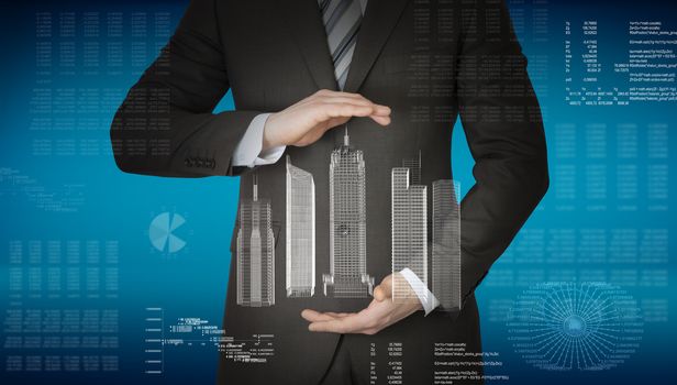 Businessman with 3d model of city in hands on abstract blue background with graphs