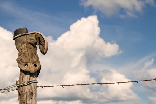 A cowboy boot upside down on a fence post in rural Kansas along a prairie with clouds in the background.