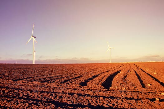 Windmill on the plowed field. Vintage sunburst picture. Alternative energy.