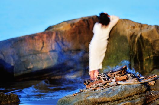 Woman in white dress near the campfire on the coast