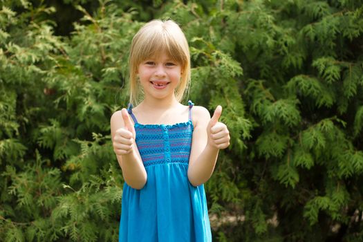 Girl 5 years old in a blue dress shows thumbs