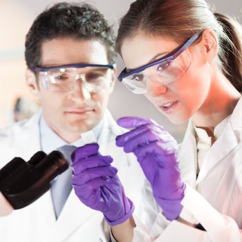 Life scientist researching in laboratory. Attractive young scientist and her post doctoral supervisor looking at the microscope slide in the forensic laboratory. Healthcare and biotechnology.