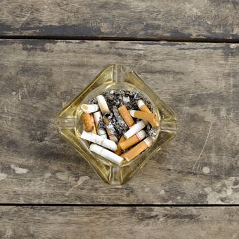 ashtray full of butt cigarettes on wooden background