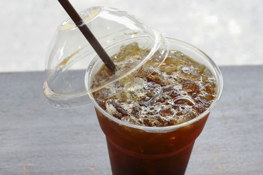 Delicious ice coffee americano with coffee glass lid and straws on wood table.