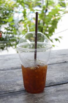 Delicious ice coffee americano with coffee glass lid and straws on wood table.